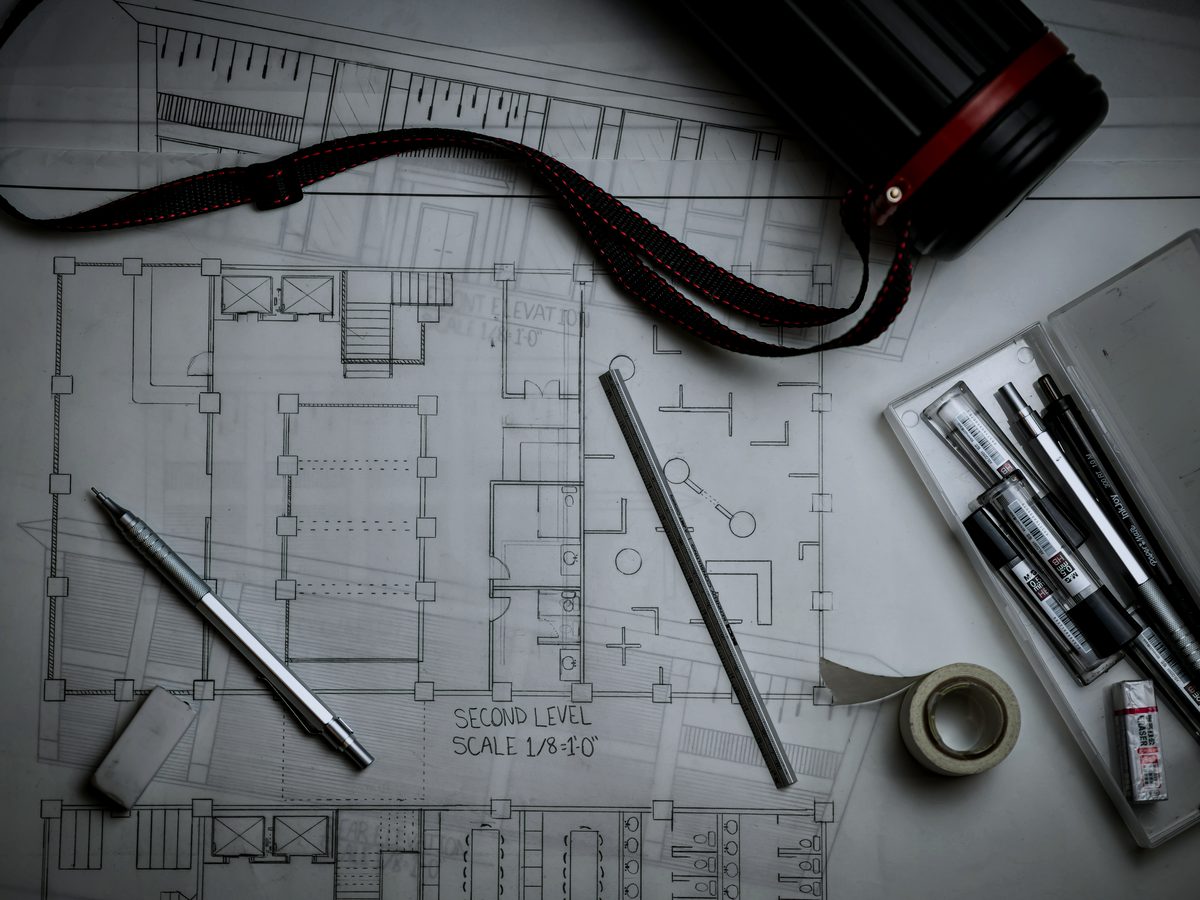 Architectural drawings on a table with drafting pencils and a metal ruler.